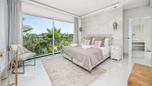 Une chambre moderne avec un grand lit, une table de chevet, une chaise et une vue sur la verdure à l’extérieur.
