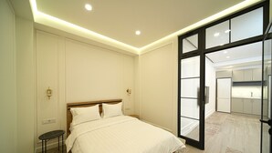 A modern bedroom with a large bed, a small side table, and a glass door leading to a kitchen area. - Stylish 2-bedroom Apartment Next to the Republic Sqaure (Yerevan)