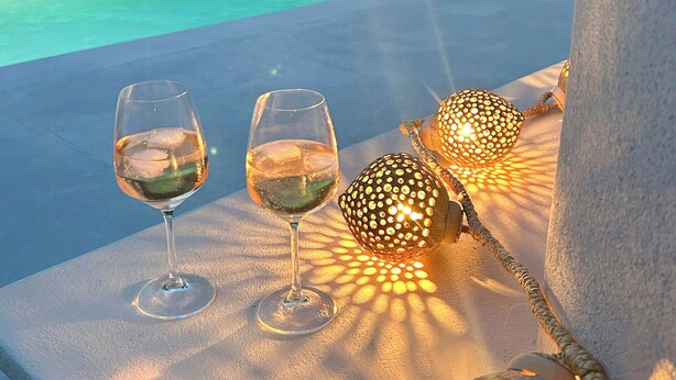 Un espace aménagé au bord de la piscine, avec des chaises longues, deux verres de vin blanc et des guirlandes lumineuses décoratives.