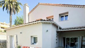 Une maison moderne dotée d’un patio comprenant un fauteuil en osier, une petite table et un banc avec des coussins.