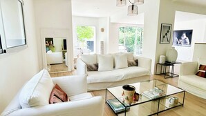 Un salon moderne avec une table basse en verre, des canapés blancs et un luminaire suspendu au plafond.