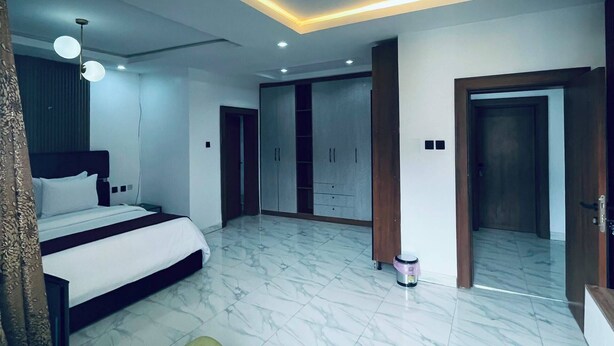 A modern bedroom with a bed, a green sofa, a wardrobe, and a bathroom visible through an open door. - Soilsmart Haven (Abuja)