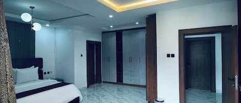 Une chambre à coucher moderne avec un lit, un canapé vert, une armoire et une salle de bain visible à travers une porte ouverte.