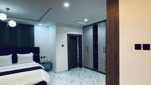 A modern bedroom with a large bed, a wardrobe, and a bathroom. - Soilsmart Haven (Abuja)