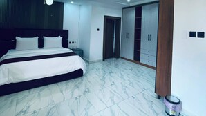 A modern bedroom with a large bed, a ceiling light fixture, and a wardrobe. - Soilsmart Haven (Abuja)