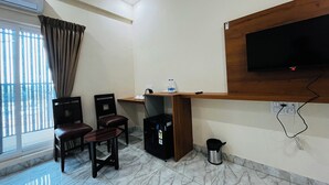 Quarto de hotel com escrivaninha, cadeiras, televisão, ar condicionado, janela com cortinas e piso de mármore.