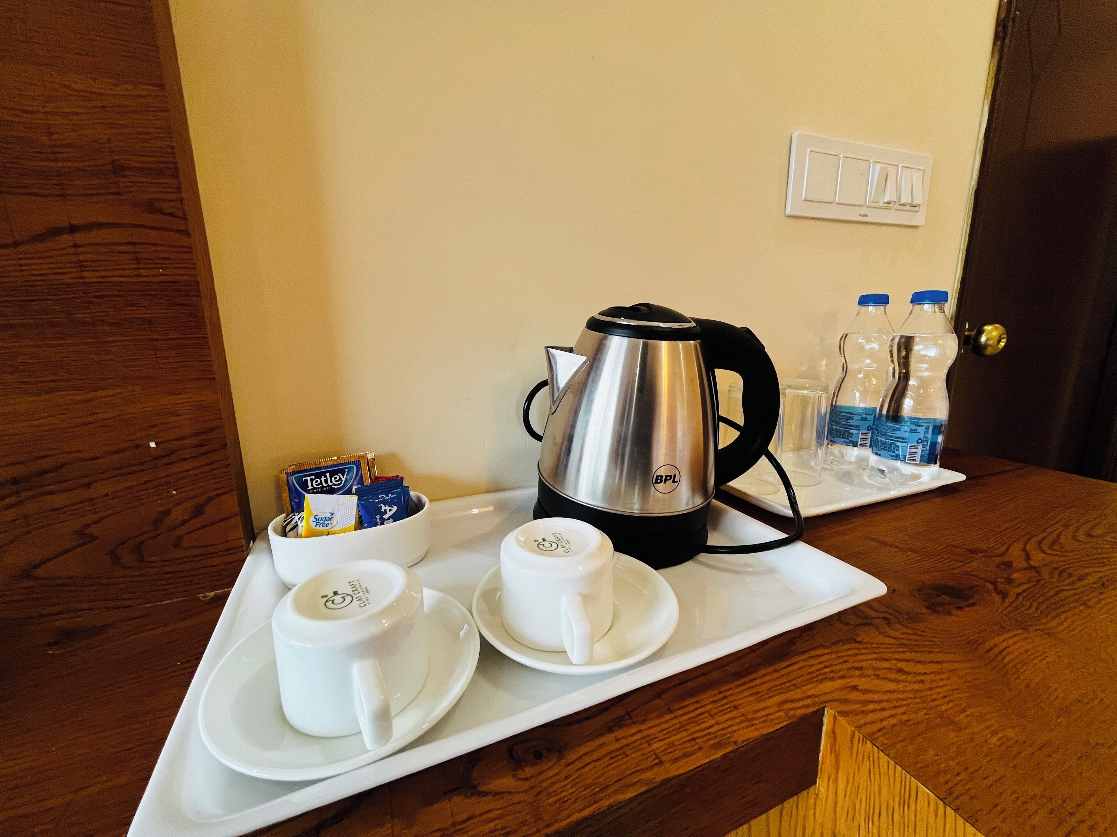 A tray with a coffee maker, cups, and Tetley tea packets on a wooden table.