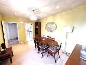 A dining area with a wooden table and chairs, a chandelier, a wall clock, and a bookshelf. - Cosy 2BDR Flat in Leytonstone near Central Line (Greater London)