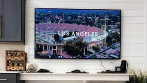 Un salon avec un téléviseur diffusant une vue de Los Angeles, un coin bar avec des tabourets, un tapis tissé et un plateau contenant une étoile de mer et des coquillages.