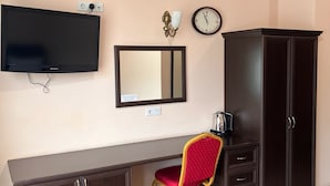 Una habitación con televisión, espejo, reloj, escritorio, silla y armario.