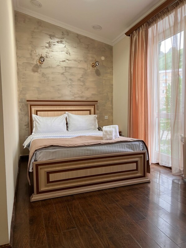 A bedroom with a wooden bed, a plain wall, and a window with curtains.
