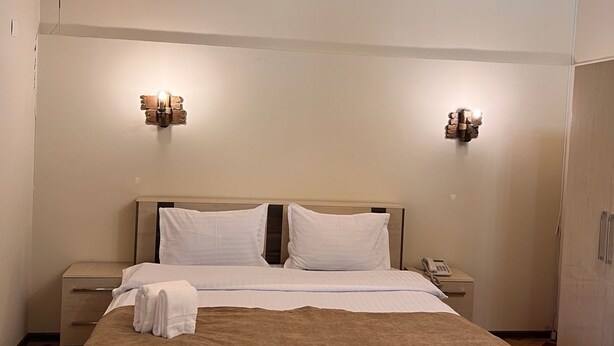Un dormitorio con techo de madera, dos lámparas de noche, una cama con cabecera marrón, una mesita de noche con un teléfono y un armario.