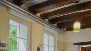 Una cocina con armarios de madera, una encimera blanca, un lavabo y un lavavajillas. Hay dos ventanas que aportan luz natural y una lámpara colgante.