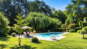 Un patio trasero con piscina, sillas de descanso y una pequeña mesa.