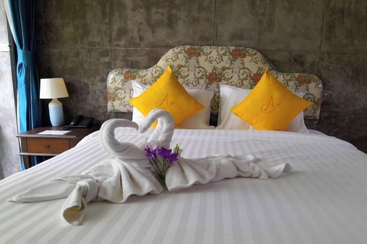 A hotel room with a bed, two pillows, a nightstand, and a lamp.