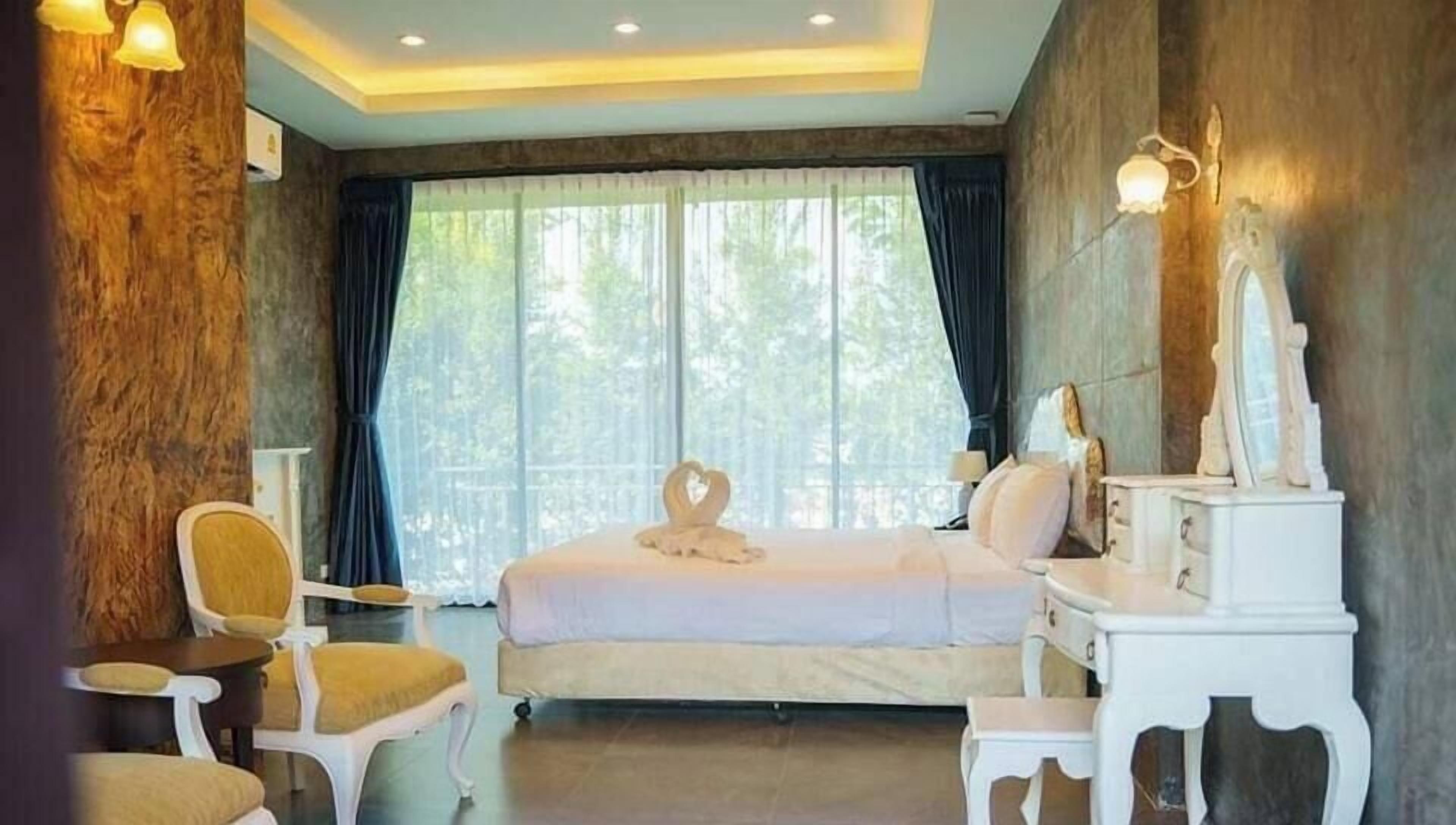 Een hotelkamer met een bed, een stoel, een klein tafeltje en een kaptafel.