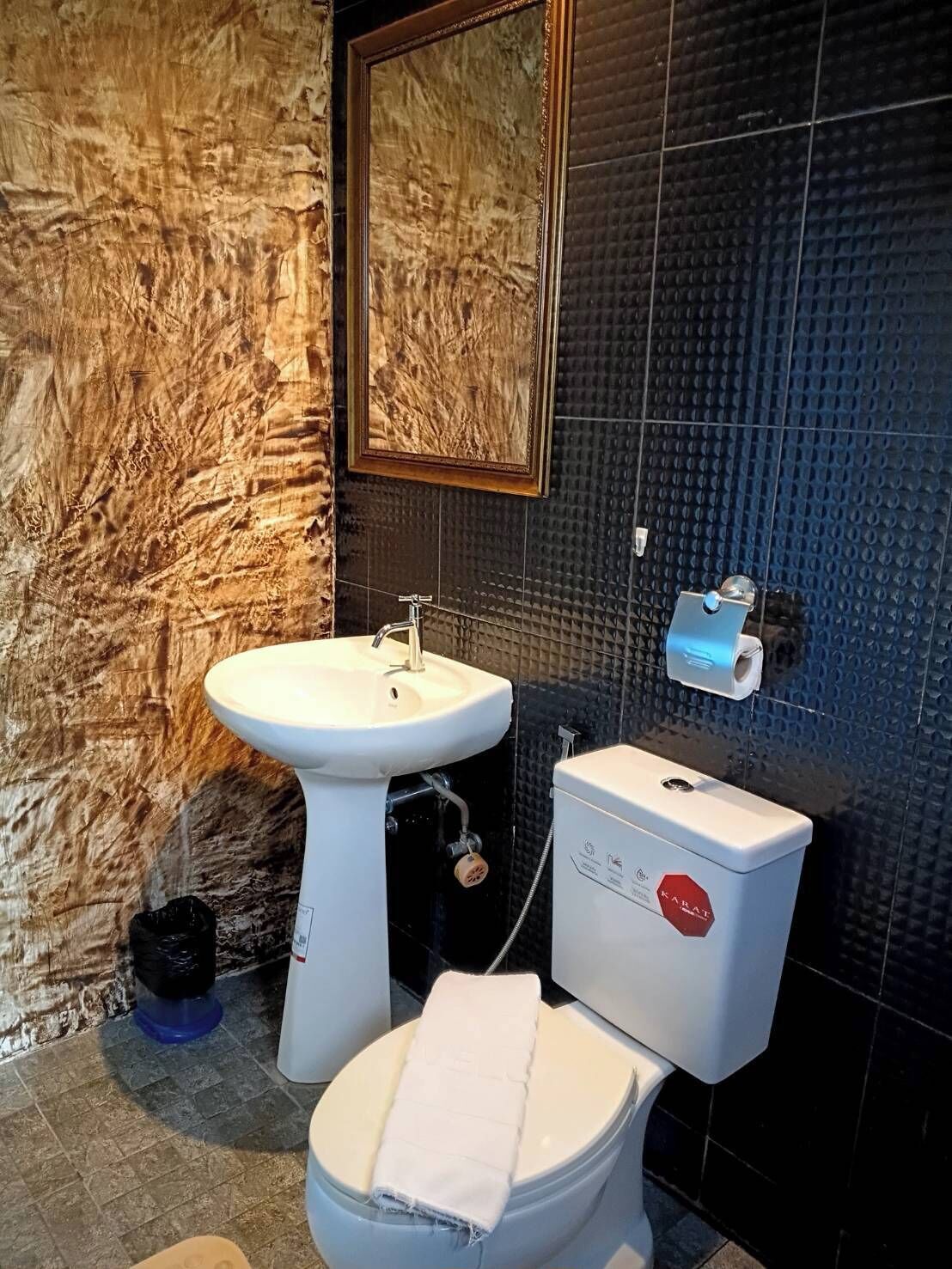 A bathroom with a marble wall, a sink, a toilet, and a mirror.