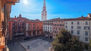 Uma praça com edifícios históricos, uma torre imponente e céu claro.