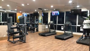 Ein Fitnessstudio mit Laufbändern, Kraftgeräten und einem Fernseher, der eine Nachrichtensendung zeigt.