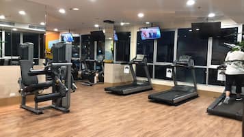 A gym with treadmills, weight machines, and a TV screen displaying a news broadcast.