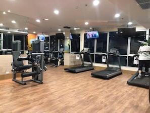 A gym with treadmills, weight machines, and a TV screen displaying a news broadcast. - Room-supalai City Resort Changwattana (Pak Kret)