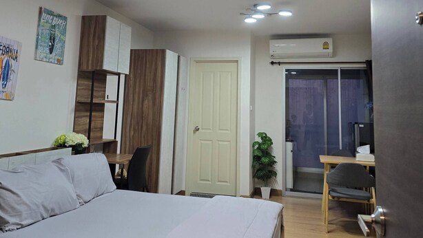 Ein Schlafzimmer mit einem Bett, einem Schreibtisch, einem Stuhl, einer Tür und einer kleinen Pflanze.