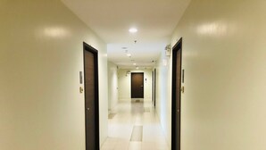 A long, narrow hotel corridor with doors on both sides, a tiled floor, and recessed lighting on the ceiling. - Room-supalai City Resort Changwattana (Pak Kret)