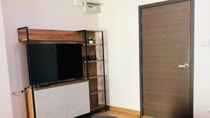 A bedroom with a bed, a TV on a wooden shelf, a door, and a wall-mounted thermostat. - Room-supalai City Resort Changwattana (Pak Kret)