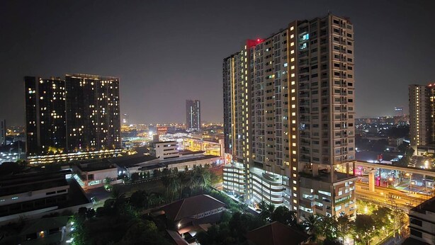 A high-rise building with multiple floors, a prominent red sign on top, and surrounding illuminated structures. - Room-supalai City Resort Changwattana (Pak Kret)