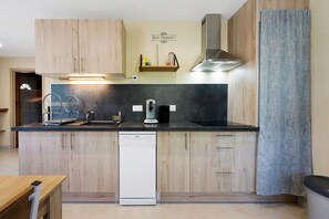 A compact kitchen with wooden cabinets, a dishwasher, a coffee machine, and a stainless steel range hood. - Apartment '4 Personnes' with Mountain View, Shared Garden and Wi-Fi (Saint-Martin-sur-la-Chambre)