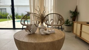 A round wooden table with decorative items, a wicker chair, a potted plant, and a wooden cabinet in a room with a view of a building outside. - Gated Luxury Villa Private Pool & 24/7 Security in Vista Cana Punta Cana. (Punta Cana)
