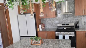 A kitchen with granite countertops, wooden cabinets, a stainless steel range hood, and hanging plants. - Gated Luxury Villa Private Pool & 24/7 Security in Vista Cana Punta Cana. (Punta Cana)