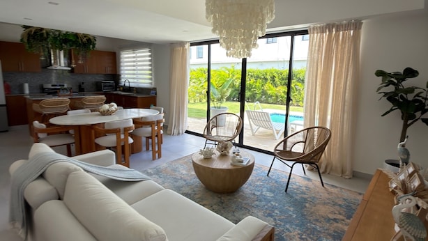 A modern living room with a white sofa, a round coffee table, and a dining area with wicker chairs. - Gated Luxury Villa Private Pool & 24/7 Security in Vista Cana Punta Cana. (Punta Cana)