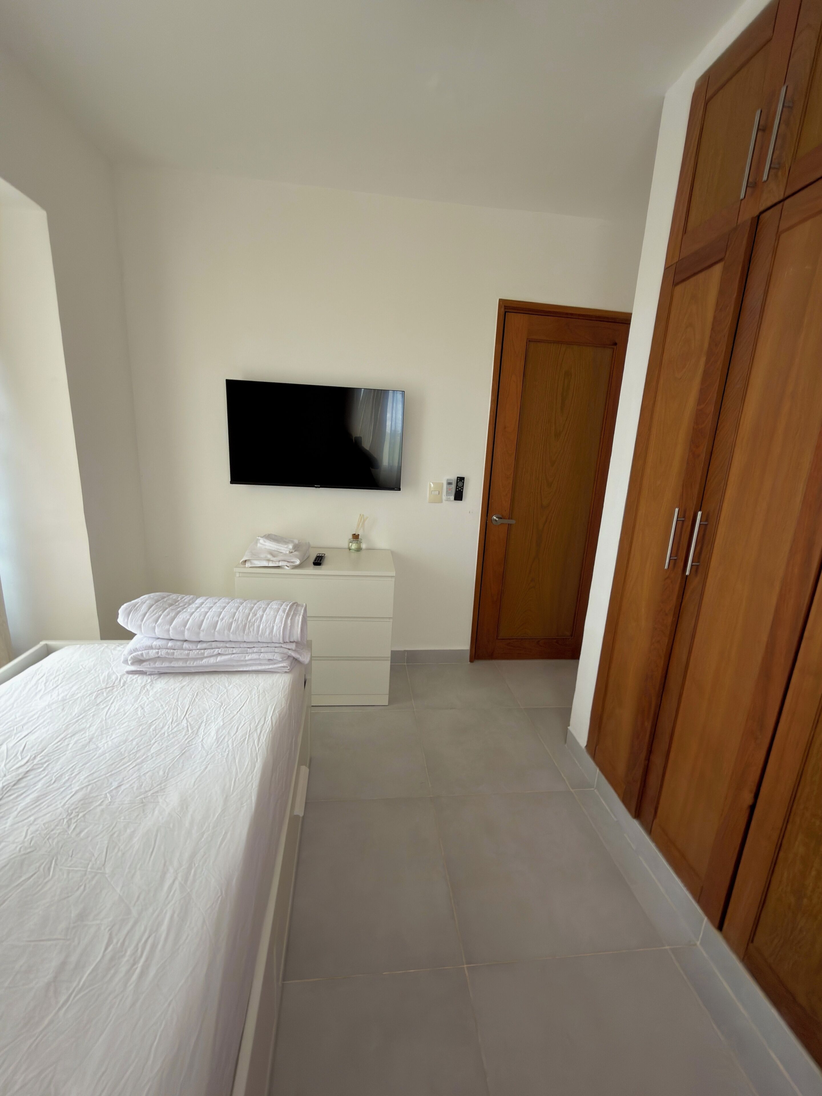 Een slaapkamer met een bed, een dressoir, een televisie en een kast.