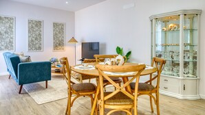 A dining area with a round table, wooden chairs, a blue sofa, a TV, and a glass cabinet with decorative items. - Silva's House, a Home in Madeira (Ponta do Sol)