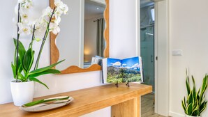 A wooden reception desk with a potted orchid, a framed photograph, and a mirror reflecting a room with a shower. - Silva's House, a Home in Madeira (Ponta do Sol)