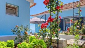 A blue building with a tiled roof, a garden with red flowers, and a concrete structure. - Silva's House, a Home in Madeira (Ponta do Sol)