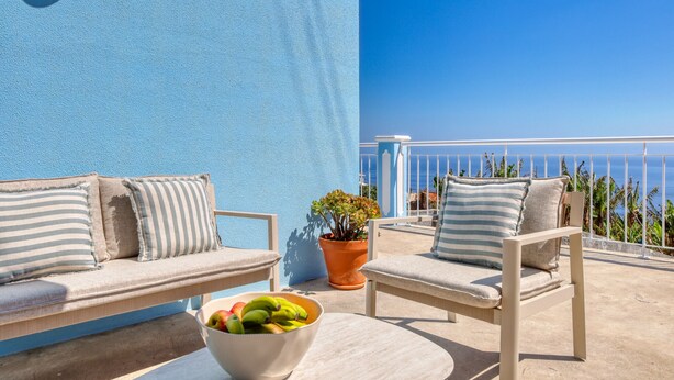 A balcony with a blue wall, two sofas with striped cushions, a potted plant, and a bowl of fruit. - Silva's House, a Home in Madeira (Ponta do Sol)