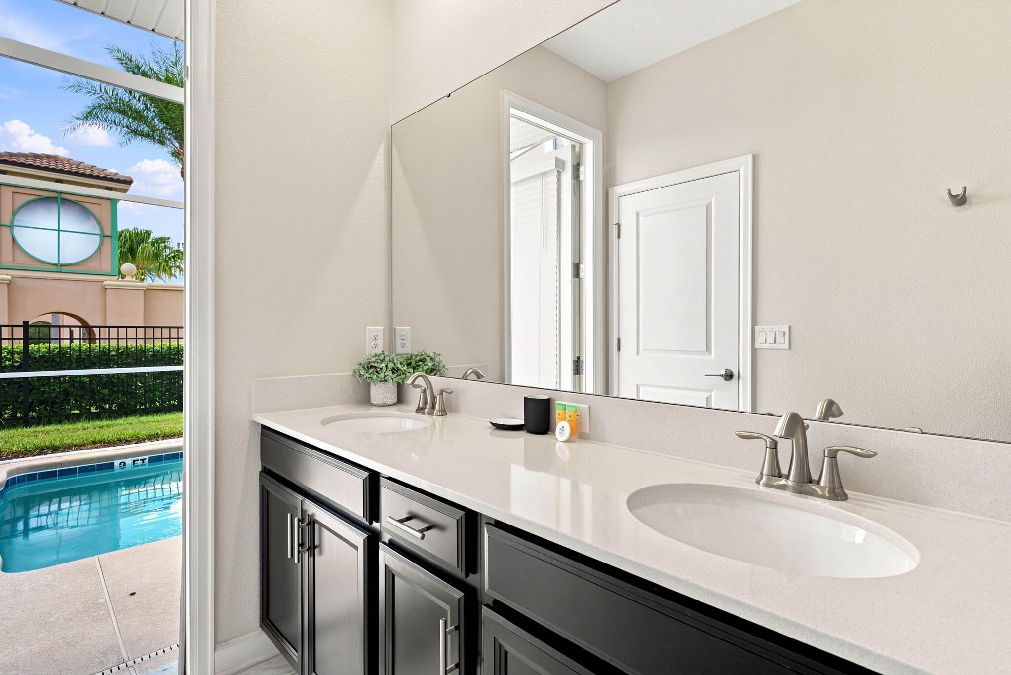 A bathroom with two sinks, a large mirror, and a view of a swimming pool.