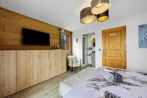 Une chambre avec une armoire en bois, un lit recouvert d’une couvre-lit à motifs, un téléviseur fixé au mur et une porte dotée d’un miroir.