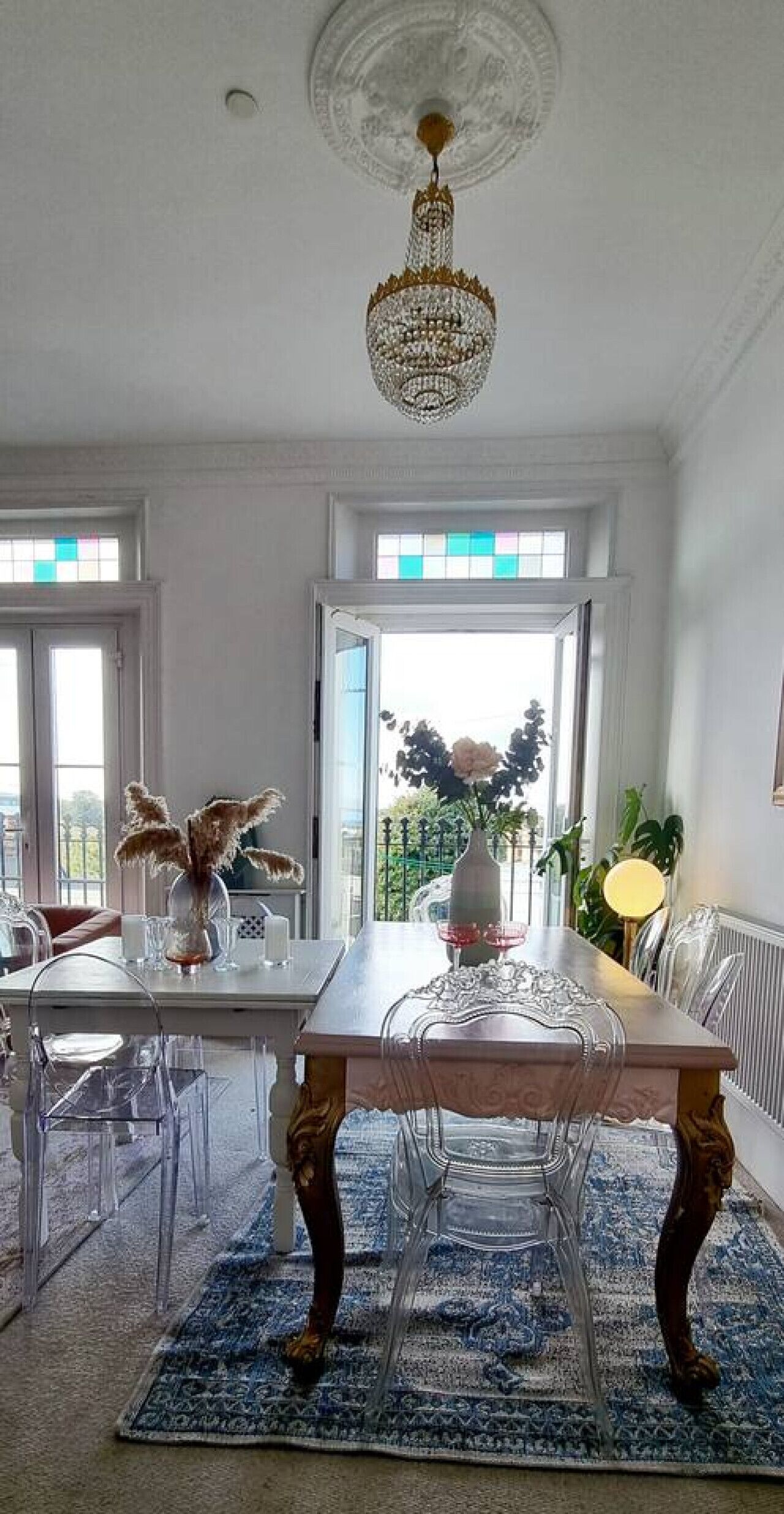 A dining area with a chandelier, a table with chairs, a vase with flowers, and a view through the open door.