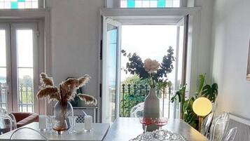 A dining area with a chandelier, a table with chairs, a vase with flowers, and a view through the open door.