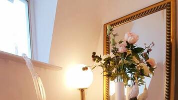 A room with a clear chair, a lamp, a mirror, and a vase with flowers.
