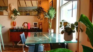 Comedor con mesa de vidrio, sillas y una planta verde grande.