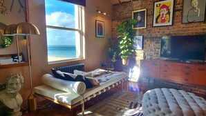 A room with a bed, a TV, a large window, and a brick wall.