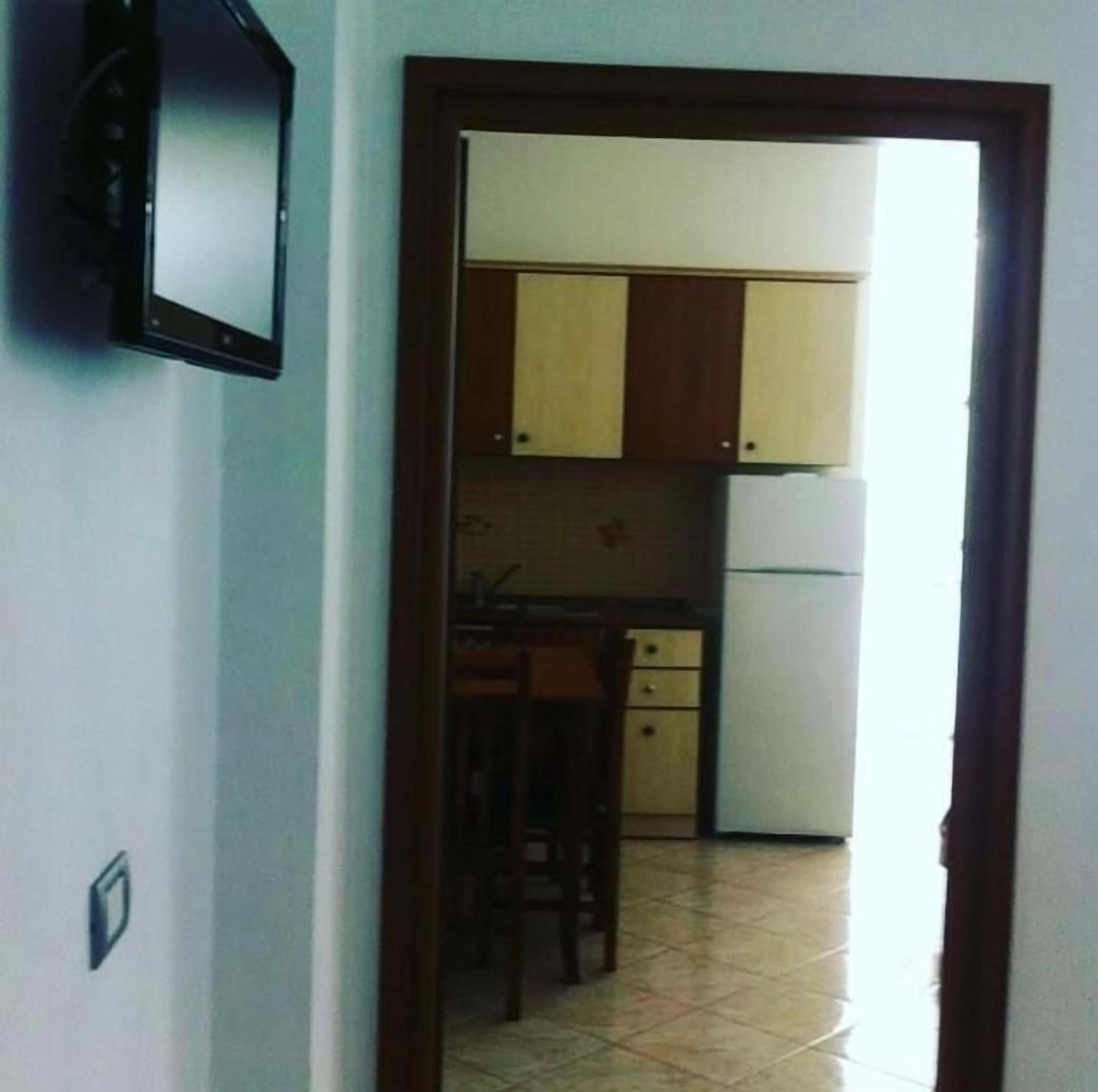 Une porte qui mène à une cuisine équipée de placards, d’un réfrigérateur et d’une chaise.