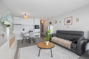 A modern living room with a grey sofa, a round coffee table, and a dining area with a white table and chairs. - 1 bedroom accommodation in De Panne (De Panne)