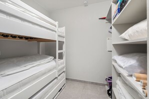 Habitación con literas, una pared blanca, una estantería con libros y una bolsa morada en el suelo.