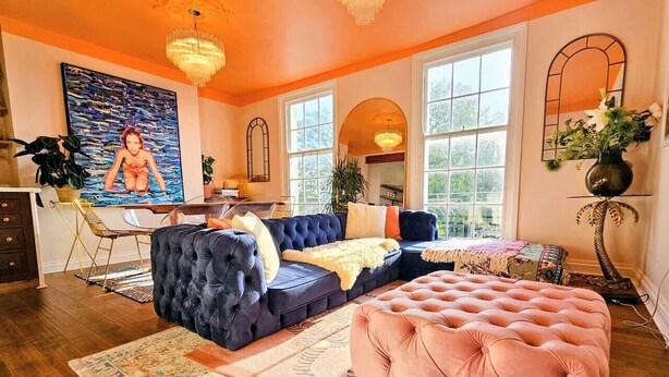A living room with a sectional sofa, ottoman, and a large painting on the wall. - 3 Bedroom Home on the Beautiful Trinity Square (Kent)