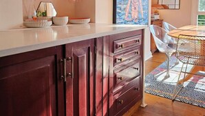A kitchen with wooden cabinets, a white countertop, and a dining area with a table and chairs. - 3 Bedroom Home on the Beautiful Trinity Square (Kent)